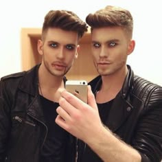 two young men taking a selfie in front of a mirror with their cell phone