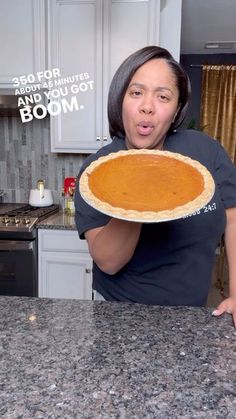 a woman holding up a pie in the kitchen