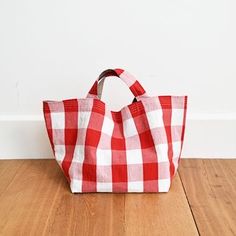 a red and white checkered tote bag sitting on top of a wooden floor