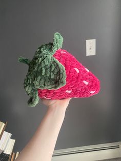 a hand holding up a crocheted strawberries toy in front of a gray wall