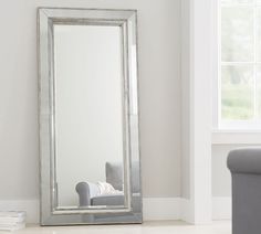 a large silver framed mirror sitting on top of a floor next to a gray chair