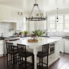 a white kitchen with black chairs and an island in front of the stove top oven