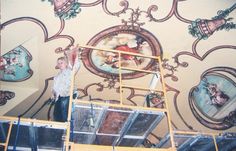 a man standing on a scaffold in front of a mural