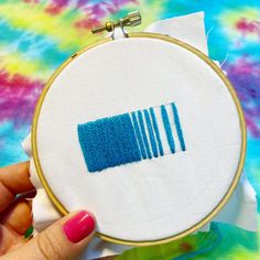 a person holding a piece of fabric in front of a cross stitching hoop with blue thread on it