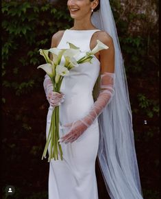 a woman in a white wedding dress holding a bouquet of flowers and wearing a veil