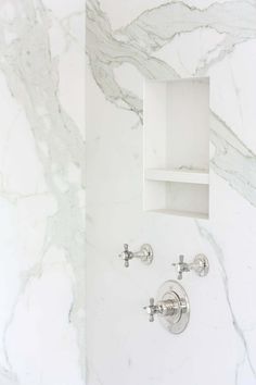 a bathroom with marble walls and flooring, two faucets on the wall