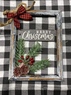 a christmas card with pine cones and evergreen leaves in a frame on a plaid tablecloth