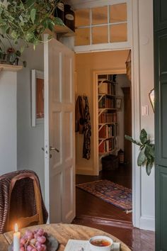 an open door leading into a living room with a table and bookshelf in the background