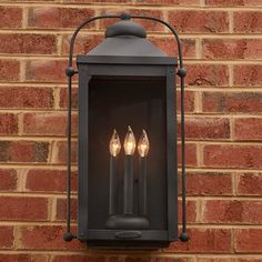 an old fashioned lantern hanging on the side of a brick building with three candles in it