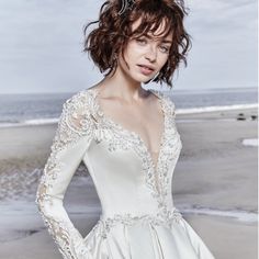 a woman in a white dress standing on the beach with her hands on her hips