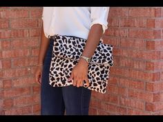 a woman is holding a leopard print clutch bag on her left hand while standing in front of a brick wall