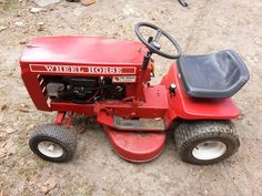 a red riding lawn mower sitting on top of a dirt field next to a black seat