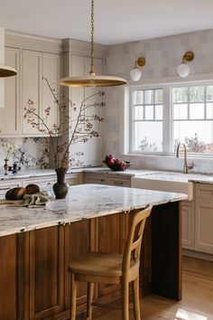 a kitchen with white cabinets and marble counter tops, two chairs at the center island