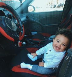 a small child sitting in the driver's seat of a car, smiling at the camera