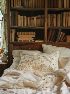 an unmade bed in front of a bookcase filled with books and other items