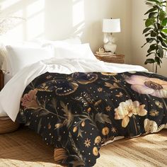 a bed with white sheets and black floral comforter on top of it, next to a potted plant