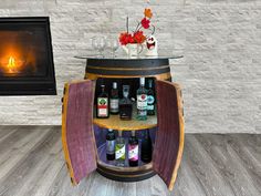 a wine barrel table with bottles and glasses on it in front of a fire place