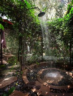 a shower head in the middle of a garden with rocks and plants around it, surrounded by greenery