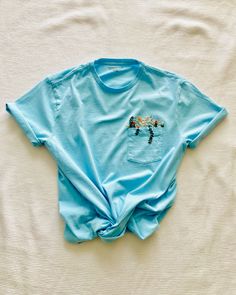 This aqua blue hand embroidered wildflower t-shirt is a perfect simple capsule piece that can be paired easily! Unisex sizing and preshrunk cotton material, so comfortable and easy to wear.  CARE:  -Turn inside out, and wash cold on delicate -Tumble dry on low, or hang dry -Turn inside out to iron Each t-shirt is hand embroidered and by nature may vary slightly from the image shown. Each embroidered piece is my own original design. This piece cannot be customized. If you would like a customized Light Blue Short Sleeve Top With Floral Embroidery, Blue T-shirt With Embroidered Text For Spring, Light Blue Embroidered Tops With Crew Neck, Blue Embroidered Relaxed Fit T-shirt, Blue Embroidered T-shirt For Summer, Blue Relaxed Fit T-shirt With Embroidered Text, Blue Relaxed Fit T-shirt With Floral Embroidery, Blue Embroidered Tops For Summer, Blue Tops With Custom Embroidery For Spring