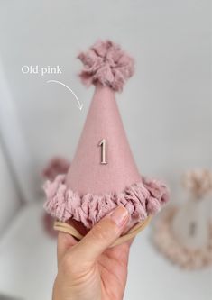 a hand holding a pink party hat with the number one on it and an arrow