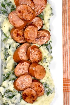 sausages and mashed potatoes on a white platter with spinach garnish