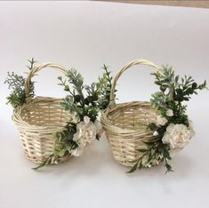 two wicker baskets with white flowers and greenery in them on a white surface