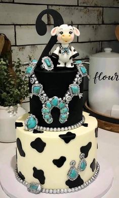 a three tiered cake decorated with black, white and teal colors has a cow on top