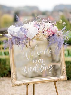 a welcome sign with flowers and greenery in front of an outdoor ceremony area for a wedding