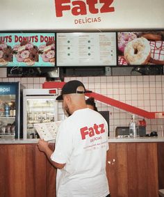 a man standing in front of a donut shop holding a doughnuts menu