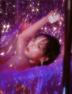 a woman laying on top of a purple bed covered in shiny sheets and pillows with her arm up