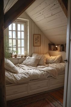 an attic bedroom with white bedding and pillows on the window sill, along with bookshelves