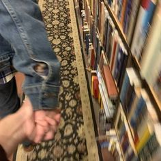 a person is picking up some books from a book shelf in a library with many rows of books on the shelves