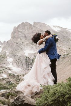 a bride and groom kissing on top of a mountain