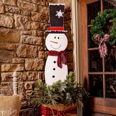 a snowman is standing next to a potted plant and wreath on the front door