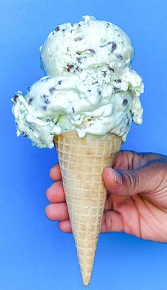 a hand holding an ice cream cone filled with chocolate chip cookies and white icing