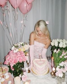 a woman sitting in front of a cake with pink flowers and balloons on the table