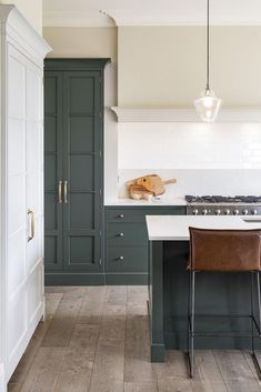 a kitchen with dark green cabinets and white counter tops is pictured in this image, there are two brown leather chairs at the center of the island