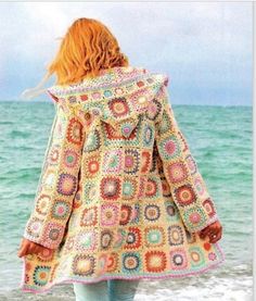 a woman standing on the beach wearing a crocheted coat with an open hood