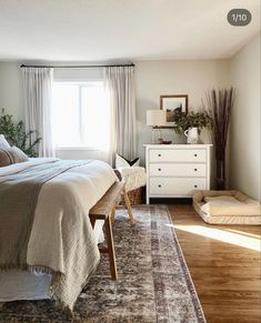 a bedroom with a bed, dresser and window in the corner next to a rug