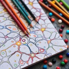 colored pencils and markers on top of a coloring book with an abstract design in the middle