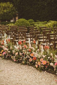 rows of chairs lined up in front of flowers on the side of a gravel road