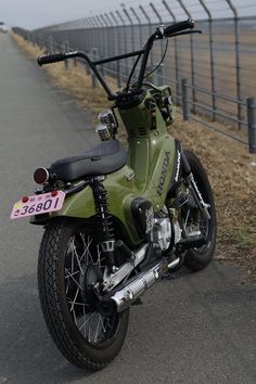 a green motorcycle parked on the side of a road next to a fence and grass