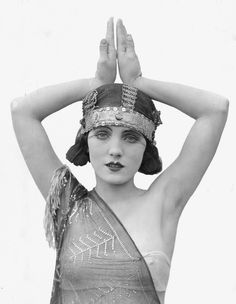 a black and white photo of a woman with her hands in the air while wearing a headdress