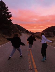 three people skateboarding down an empty road at sunset