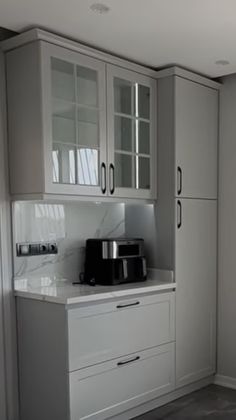 a kitchen with gray cabinets and white counter tops, along with a black coffee maker