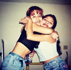 two young women hugging each other in front of a wall