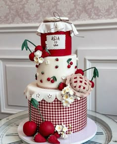 a three tiered cake decorated with cherries and flowers on a table next to a wall