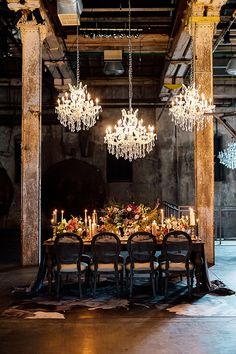 a dining room table with chandeliers hanging from the ceiling and candles on it