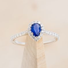 a diamond and blue sapphire ring sitting on top of a wooden stand