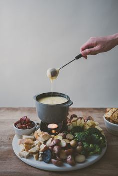 a person is dipping something into a pot on top of a plate filled with food